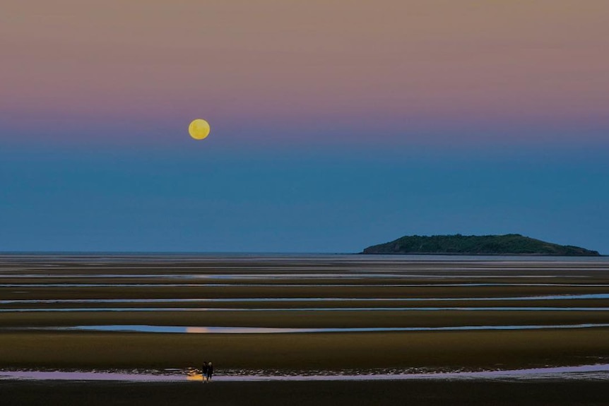 A full moon with sand banks in the foreground.