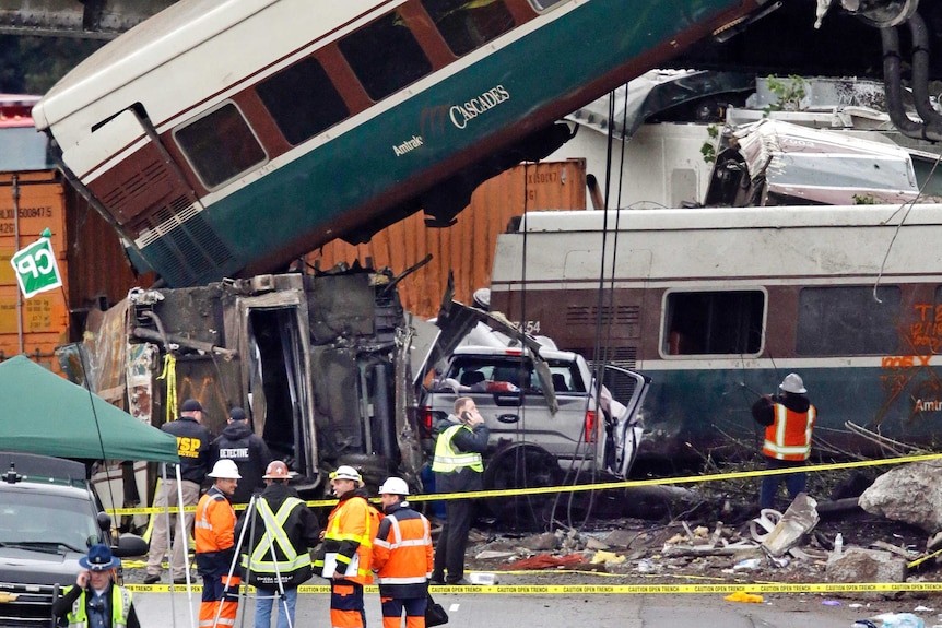 A train carriage hangs off a bridge and on top of a vehicle.