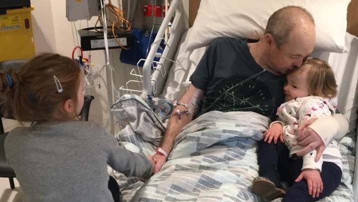 Jarrod Lyle lays with his daughters in a hospital bed.