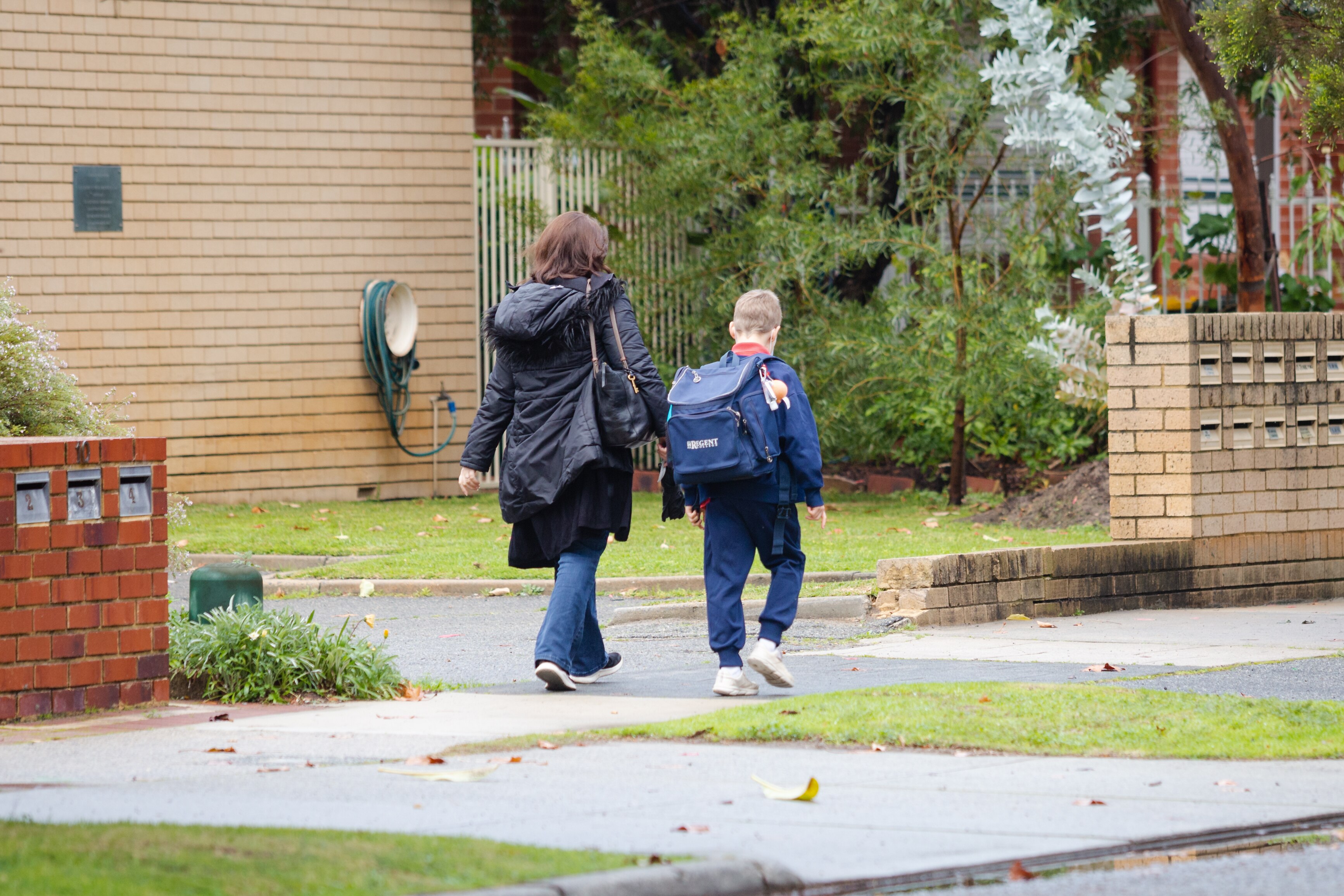 A young male student with a backpack walks along a footpath next to a woman.