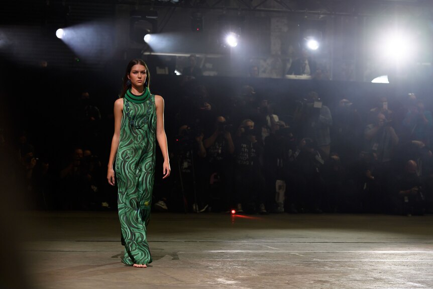 A model in a green woven dress walks a runway.