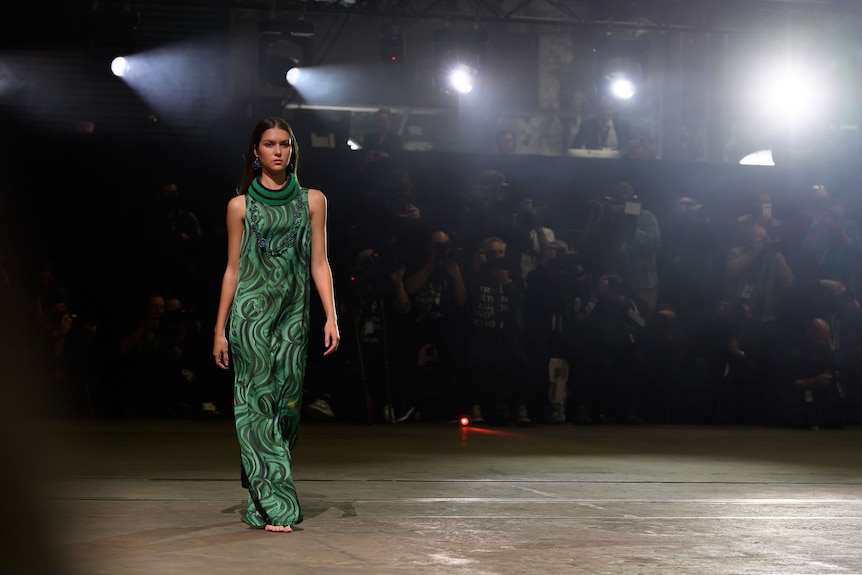 A model in a green woven dress walks a runway.