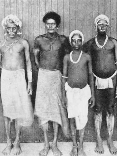 Five men in traditional islanders dress poses for a photo in front of a wooden wall