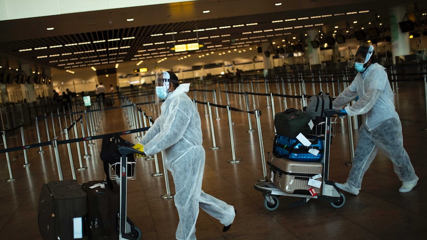 Passengers wearing full protective gear oush their luggage to check in at Brussels airport.