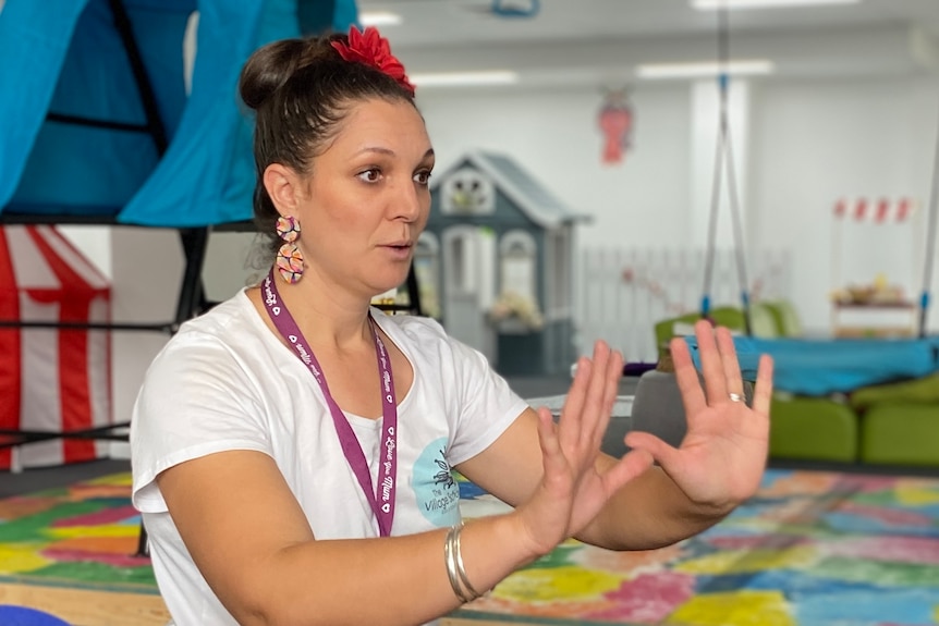 A teacher with a red flower in her hair gestures.