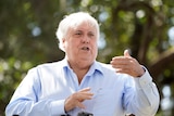A man with white hair wearing a business shirt in mid-conversation