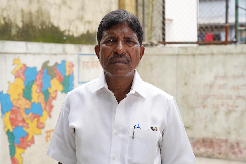 A man in a white shirt stands in front of a map of India 