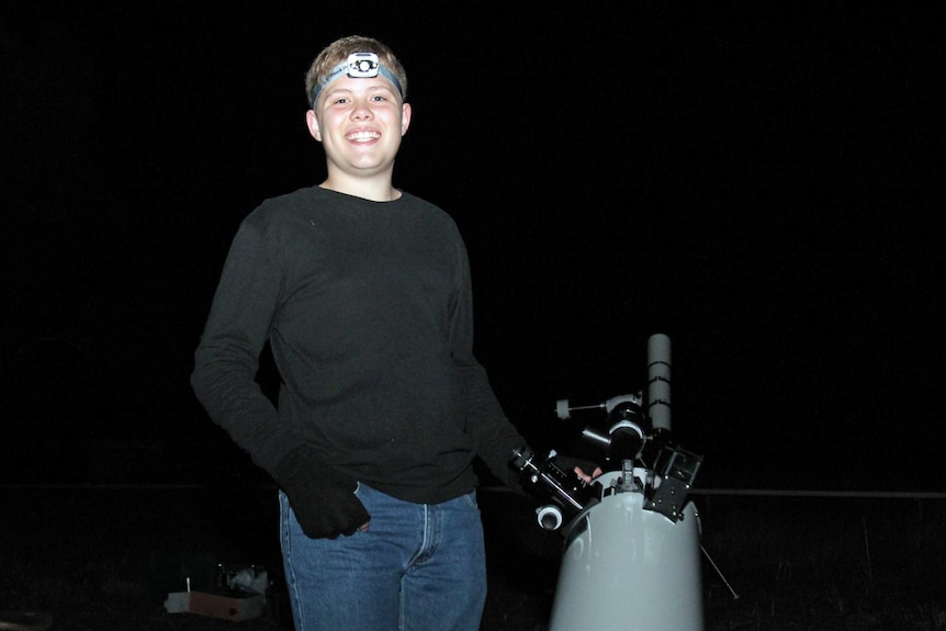 Teenager smiling standing next to a telescope