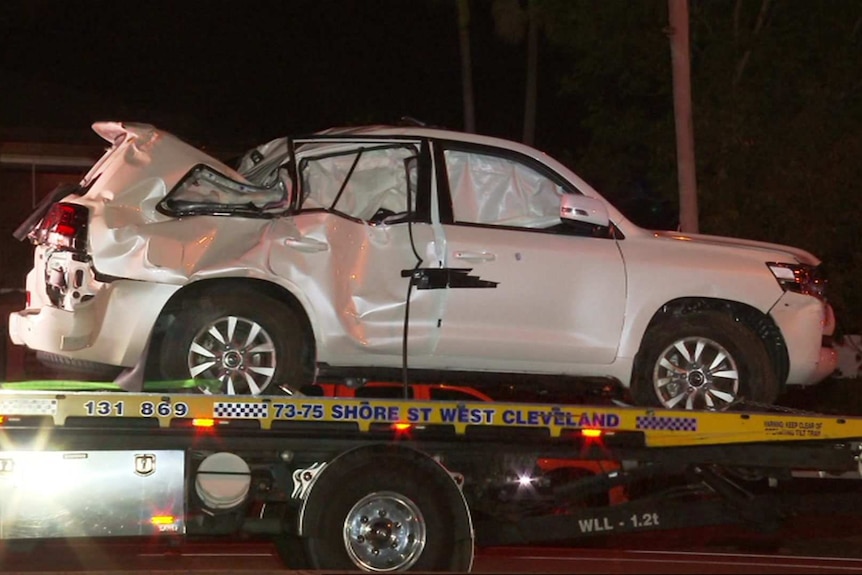 A crumpled white 4WD on the back of a tilt-tray tow truck.