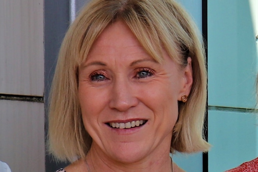 A woman in her mid to late 40s with short blonde hair looking off camera and smiling.