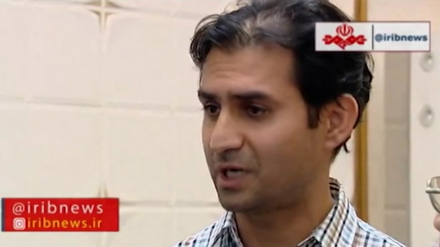 Reza Dehbashi Kivi wearing a check shirt, speaking to media in front of a cream coloured building.