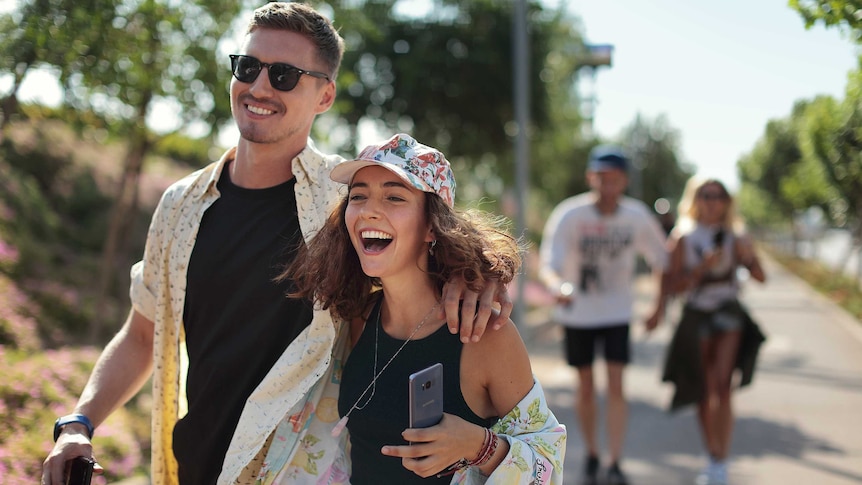 A young man and woman walk down the street holding their phones for a story about lending money to friends