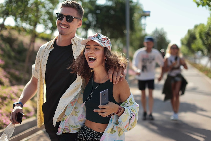 A young man and woman walk down the street holding their phones for a story about lending money to friends