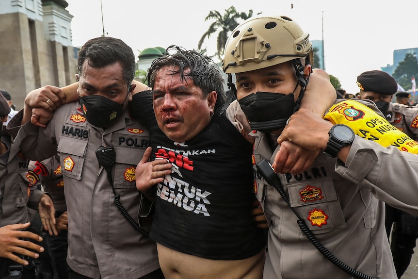 Un homme est sorti d'une foule par des fonctionnaires avec un visage blessé .