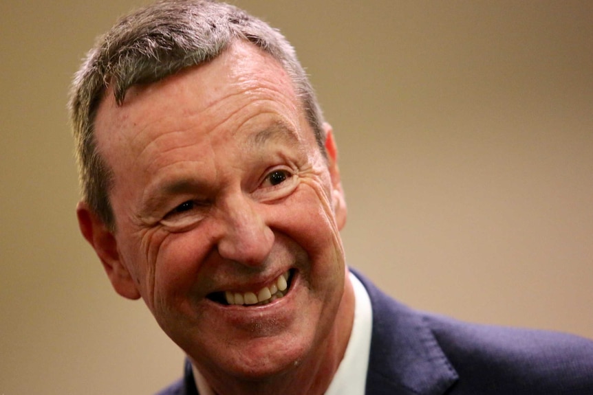 Neale Daniher, dressed in a suit, smiles and looks to the side.