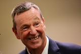 Neale Daniher, dressed in a suit, smiles and looks to the side.
