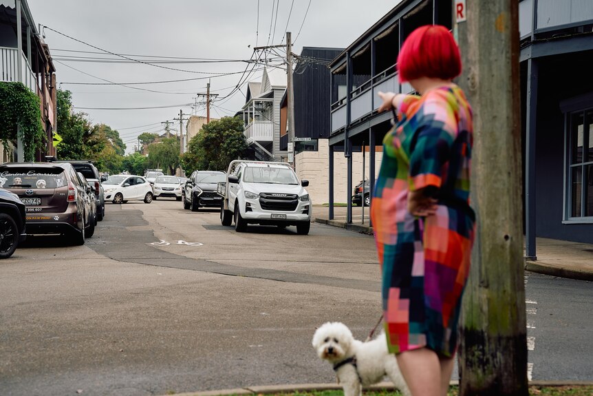 Woman with red hair and white fluffy dog pointing at cars on her street