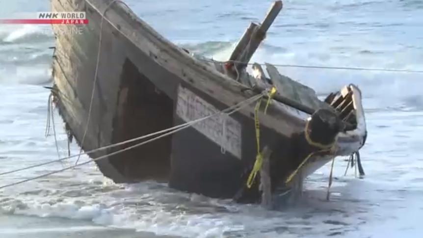 The broken off bow of a wooden boat sits on the shorelines on Japan's coastline, tied down with rope.