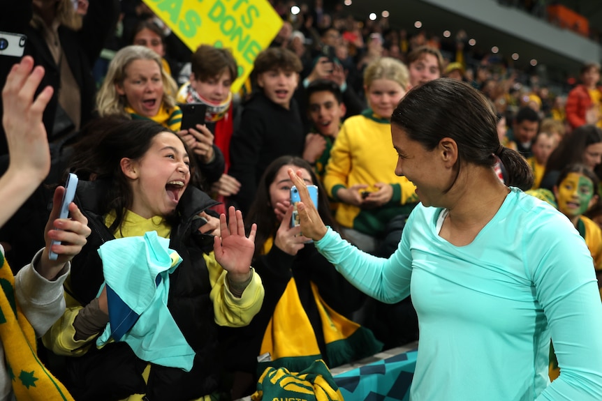 A young girl in a crowd of football fans waving at Sam Kerr