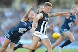 A Collingwood AFLW player tries to get a kick away as a Carlton defender reaches out to tackle her from behind. 