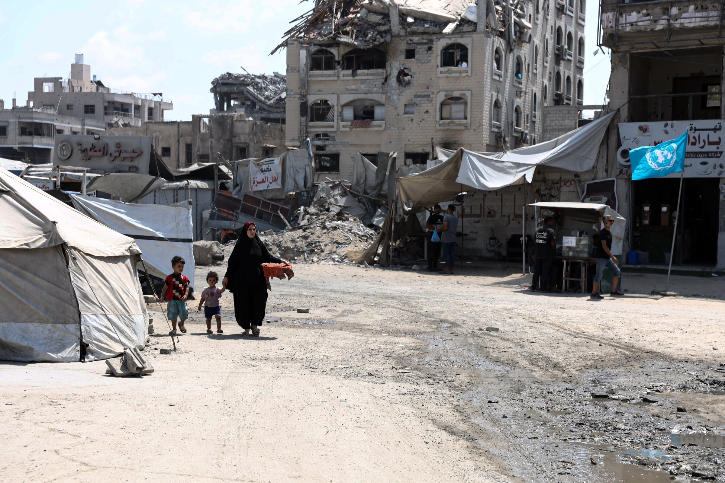 A photo of a woman holding the hand of two children as they walk through a war-torn street. Buildings around her have crumbled.