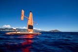 A bright orange sail drone on the water with a city in the distance