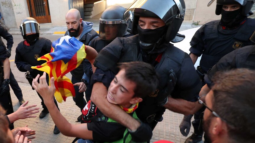 A police officer has a young man holding a Catalan flag in a headlock.