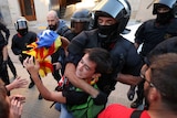 A police officer has a young man holding a Catalan flag in a headlock.