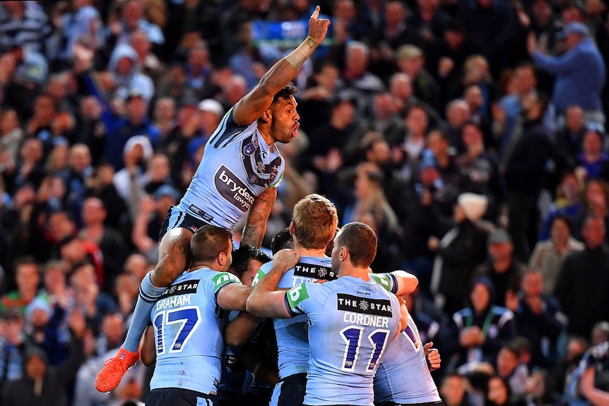 Josh Addo-Carr leaps above NSW players in embrace.