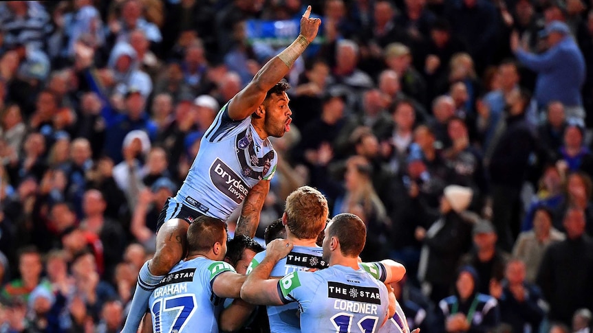 Josh Addo-Carr leaps above NSW players in embrace.
