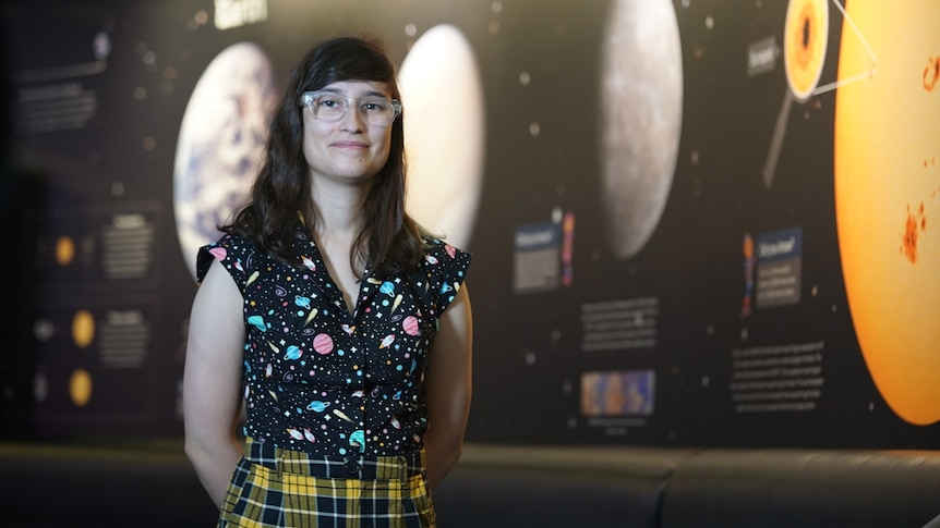A woman in front of a poster of various astronomical features