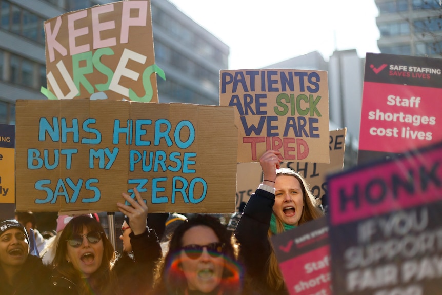 A group of nurses striking holding placards the front one reads "NHS hero but my purse says zero"