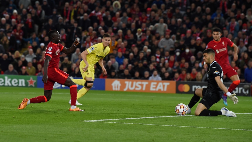 A Liverpool striker watches as his shot slides past the goalkeeper whose body is spread to stop him.