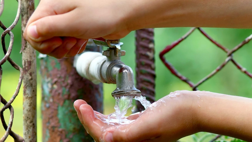 Close up child hands with water drops from old grunge brass faucet on green bokeh background