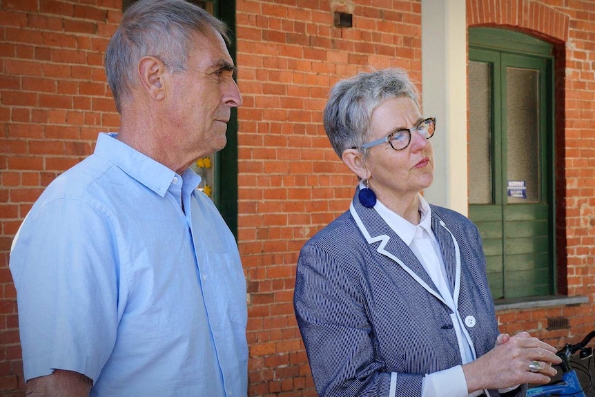 A man in a blue shirt and short brown hair and a lady with white hair and a vibrant blue jacket talk to a person off camera