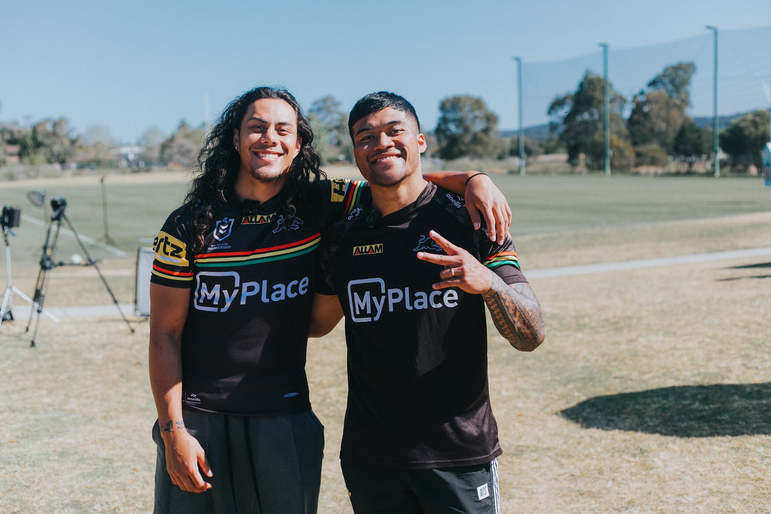 Two boys in black rugby league jerseys with red, yellow and green smile for the photo with their arms around each other 