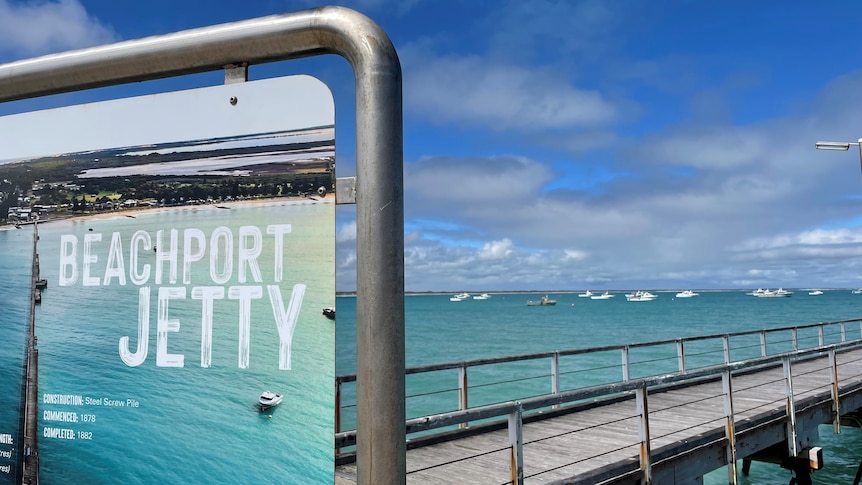 A jetty extending over the ocean with a sign in the foreground that says Beachport jetty. 