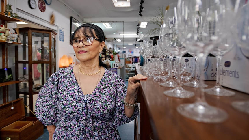 Feliota Fahey stands next to a shelf with glasses on top of it.