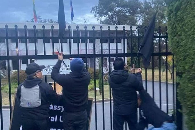 Three protesters with flags try to attach flags to the gate at the Myanmar embassy in Canberra. 