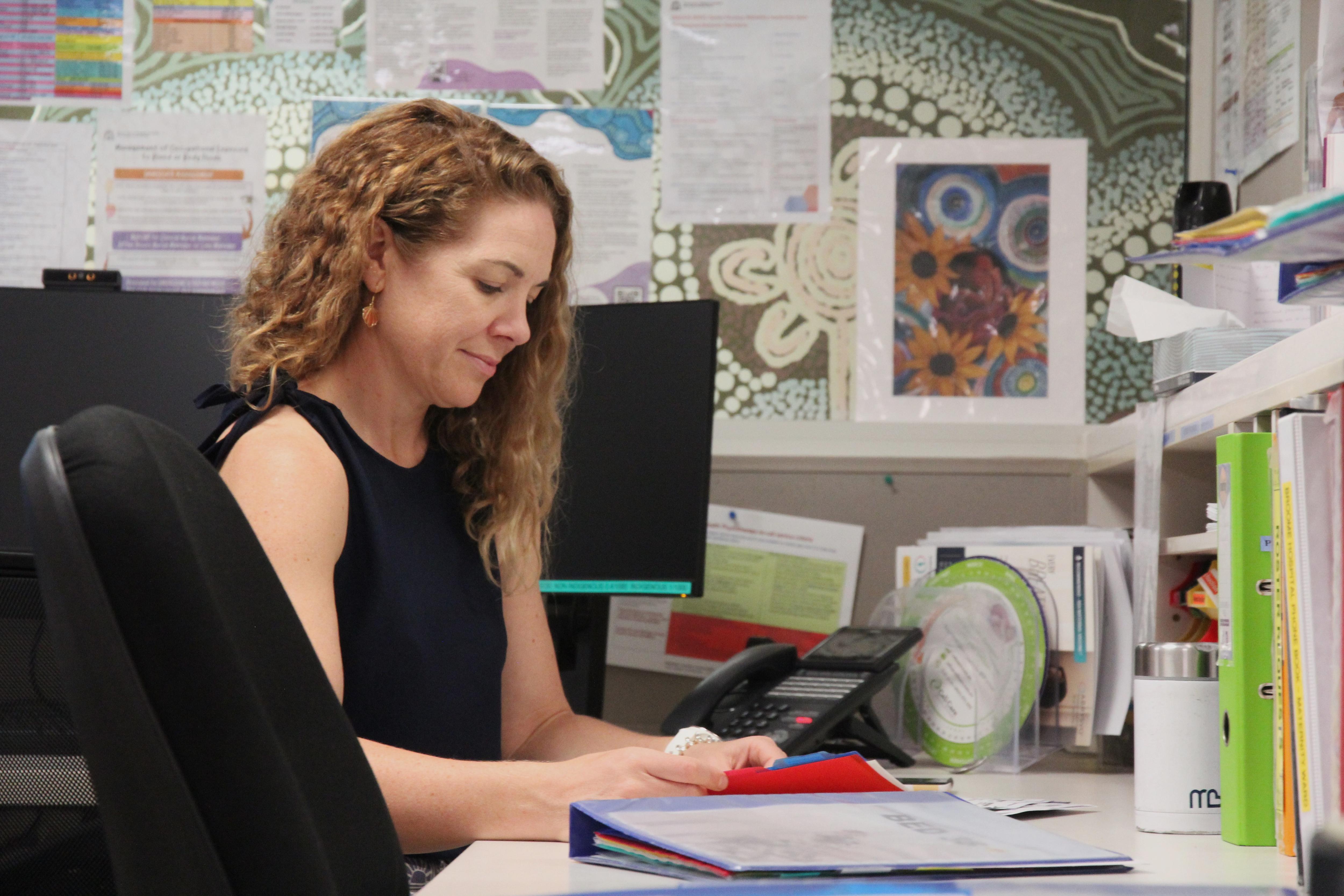 Una mujer sentada en un escritorio y hojea una carpeta