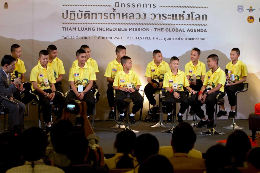 Boys in yellow t-shirts sit on a stage.