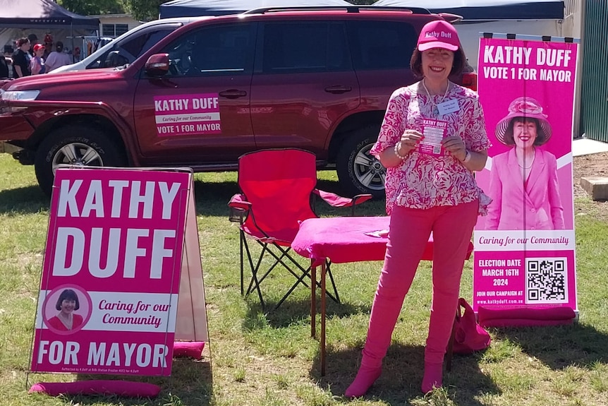 A woman in an all pink outfit stands in front of pink themed election signage