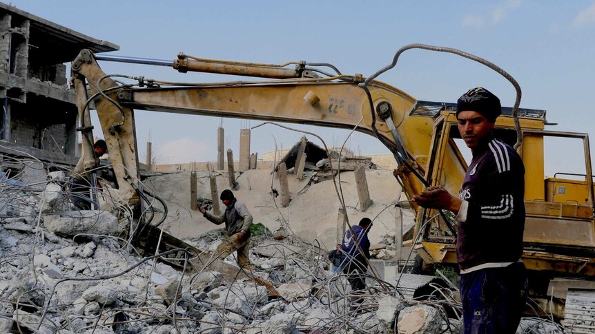 Men work with a bulldozer to clear rubble