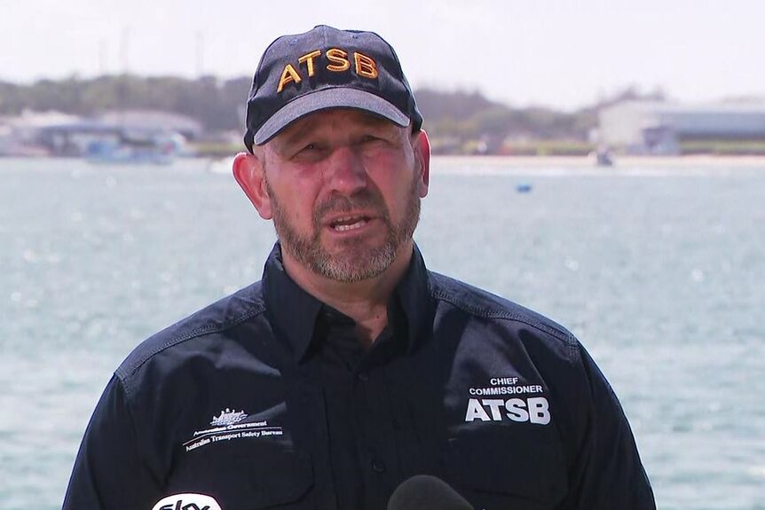 A man wearing a navy coloured ATSB and cap speaking to media at the Broadwater on the Gold Coast. 