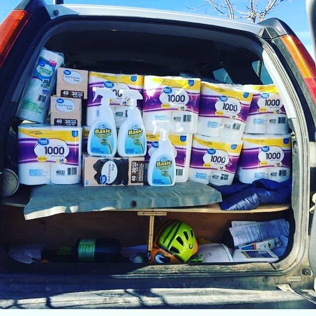 The boot of a large car is fully loaded with stacks of toilet paper and bottles of cleaning equipment.