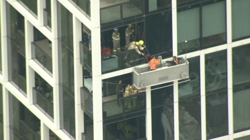 Firefighters reach out the window of a high-rise apartment building to help workers off a suspended platform.