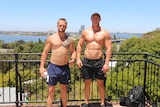 Two men with their shirts off pose for a photo at a park