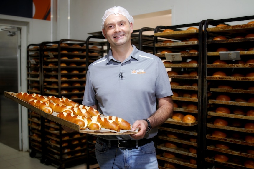Glenn holds a tray of bread and wears a hair net