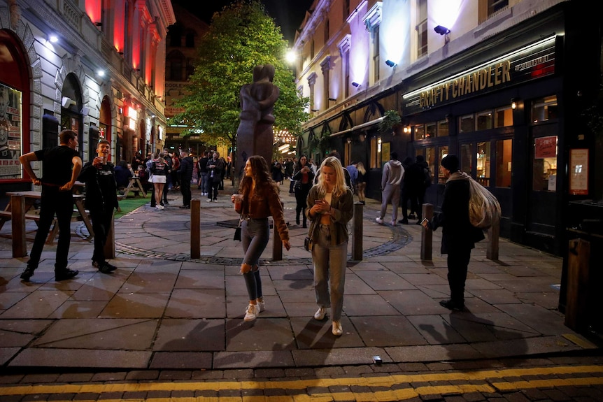 People walk at night in a square in Liverpool, England.