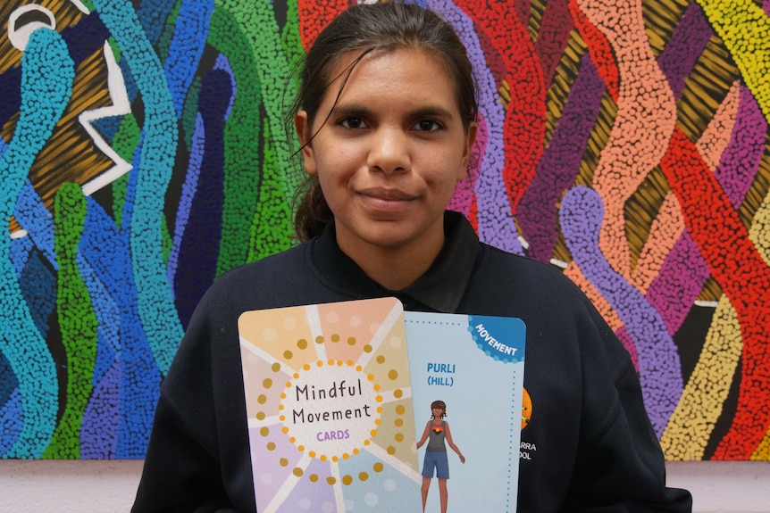 A young girl holding Mindful Movement yoga cards she designed.